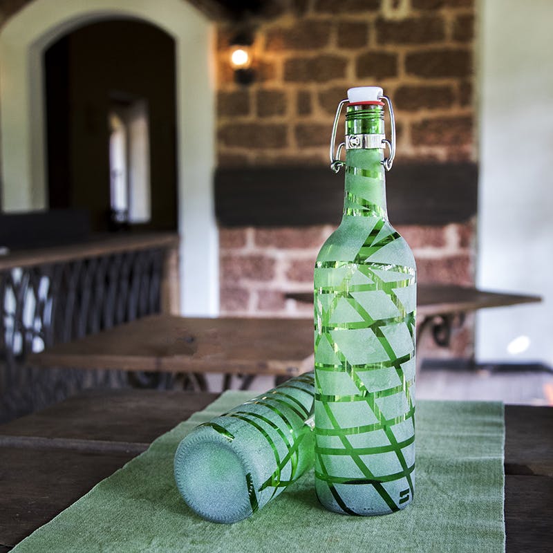 Green,Bottle,Beer bottle,Glass bottle,Wine bottle,Grass,Table,Glass,Home accessories,Drink